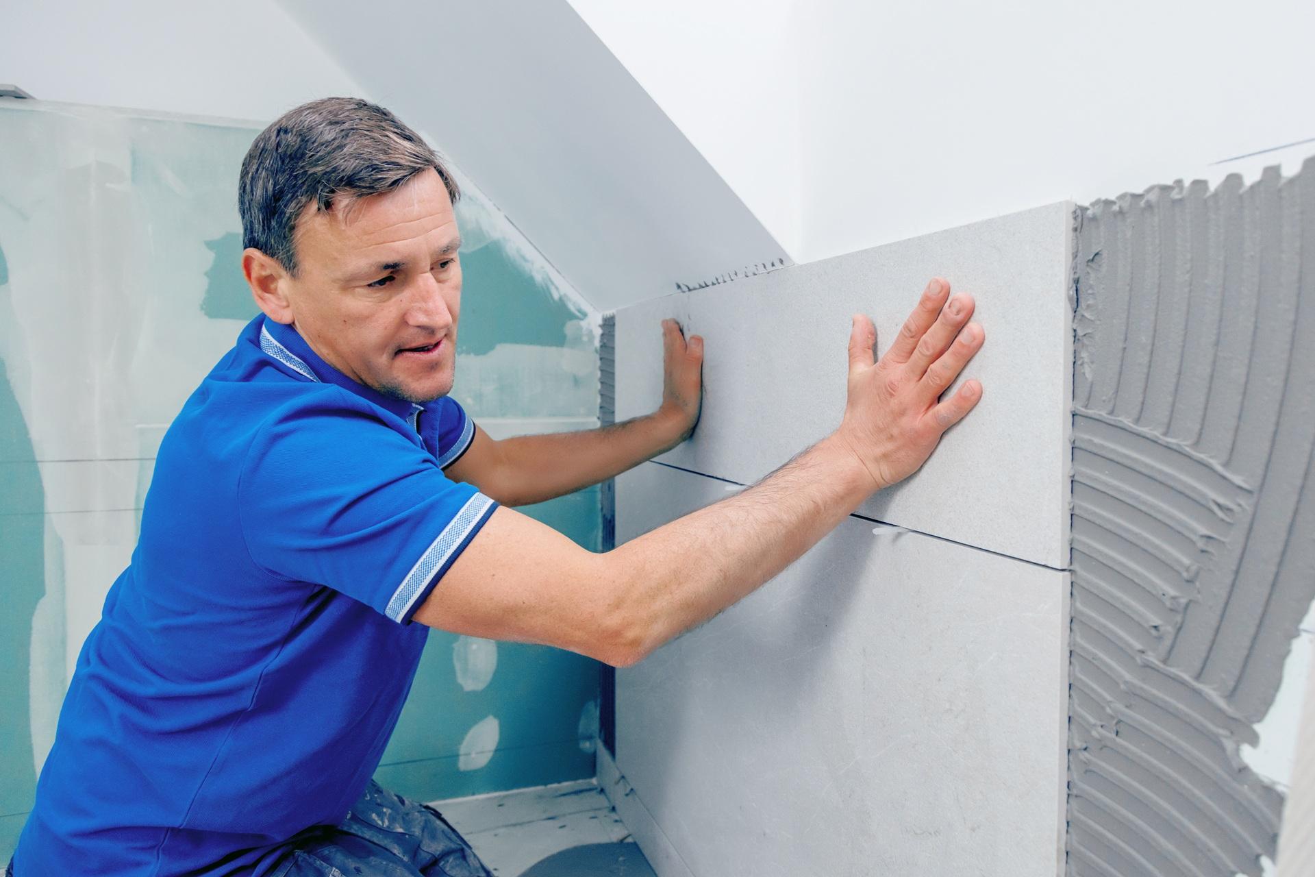Handwerker setzt Fliesen an Wand | professionelle Terrassenüberdachung Köln