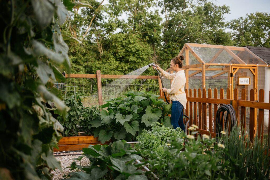 Frau bewässert Hochbeet im Gemüsegarten mit Wasser aus Regenzisterne – nachhaltige Gartenpflege